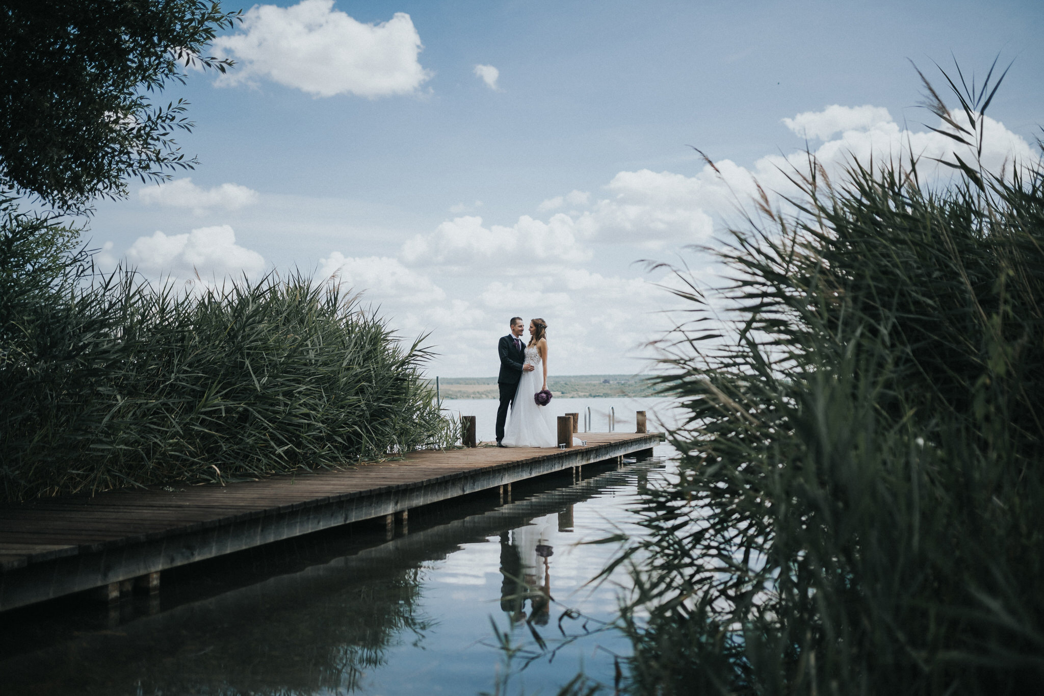 Idyllisches Brautpaarfotoshooting am Seeufer – Die Liebe des Paares wird in romantischen Bildern eingefangen, während sie entlang des Ufers spazieren und den Zauber des Augenblicks erleben.