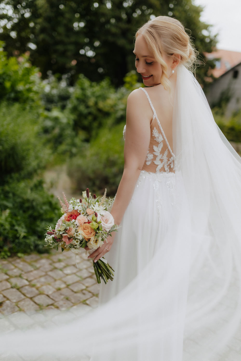Zarter Moment mit wehender Schleppe und Brautstrauß im Garten
