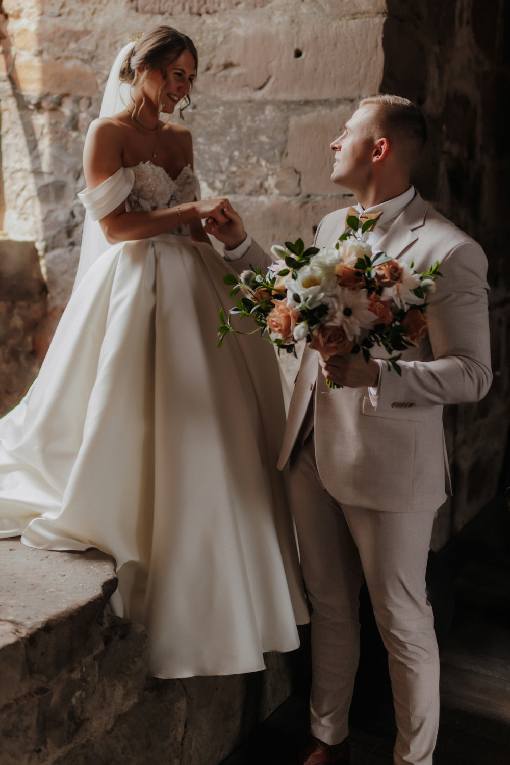 Bräutigam hält Blumenstrauß, Braut steht im Licht der Burg Hardegsen