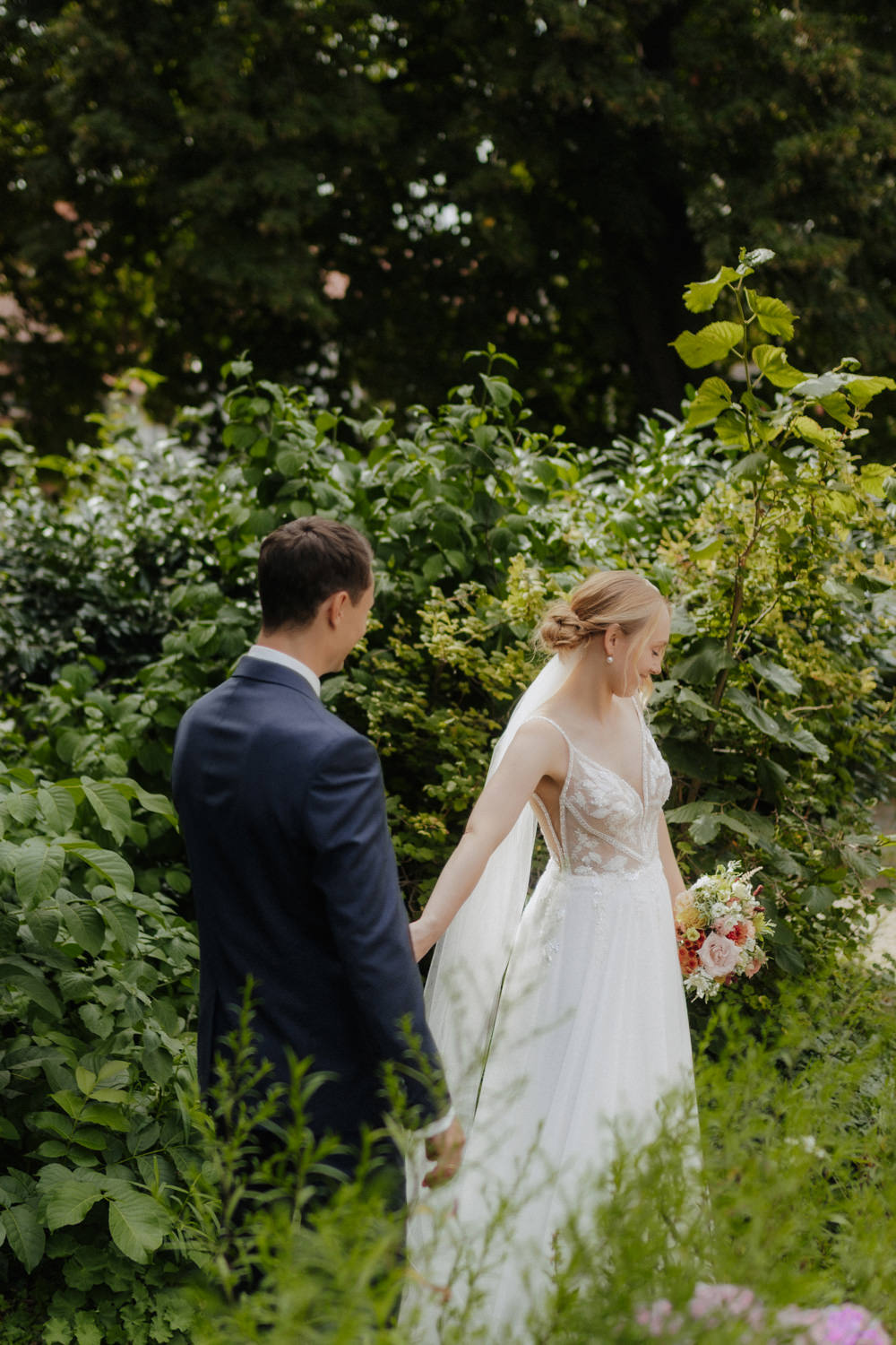 Braut führt Bräutigam durch grünen Garten bei einer Hochzeit in Göttingen