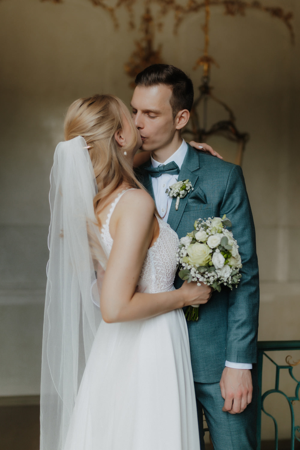 Brautpaar-kuesst-sich-im-Schloss Braut küsst Bräutigam, Hochzeitsstrauß mit weißen Rosen im Fokus