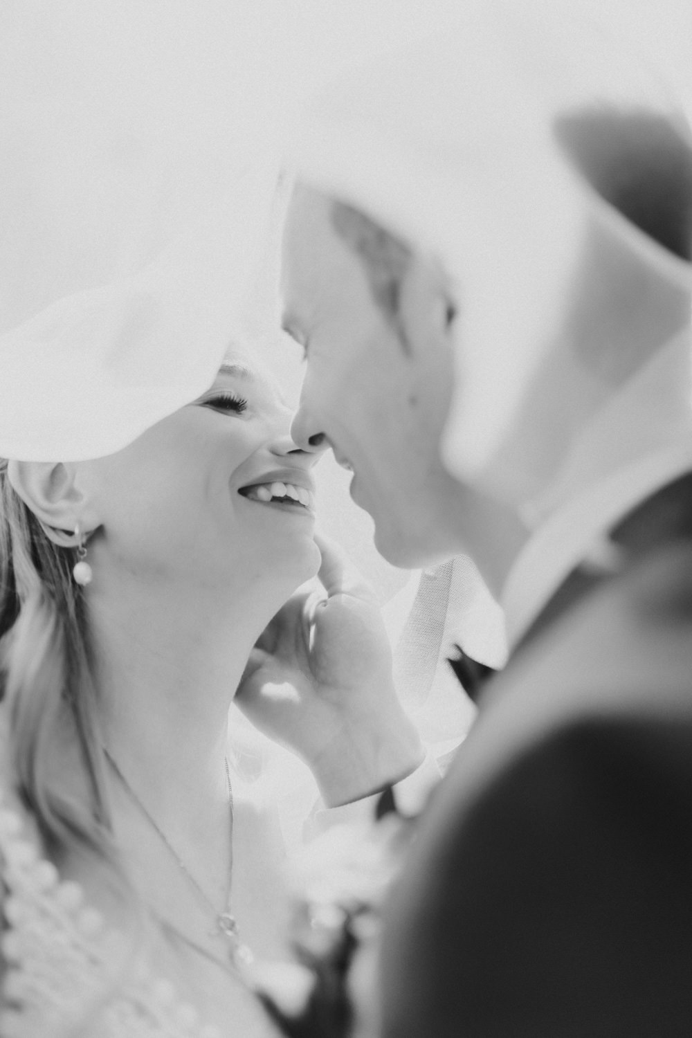 Brautpaar-kuesst-sich-unter-Schleier Zärtlicher Moment unter dem Schleier, Hochzeitsfoto in Schwarzweiß