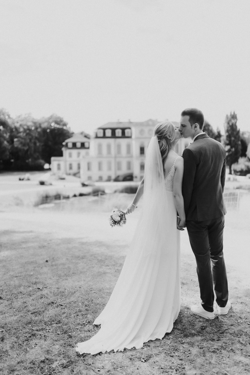 Brautpaar-kuesst-sich-vor-Schloss Brautpaar küsst sich mit Blick auf Schloss Wilhelmsthal in Schwarzweiß
