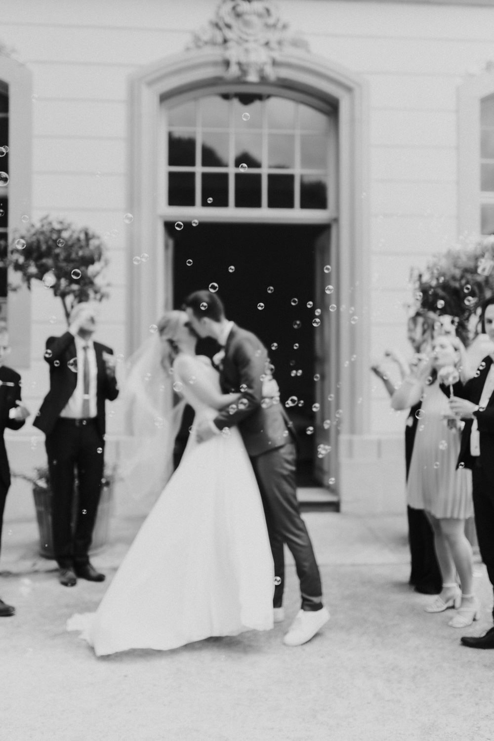 Brautpaar-kuesst-sich-vorm-standesamt Schwarzweißaufnahme vom Hochzeitskuss mit Seifenblasen vorm Schloss in Kassel