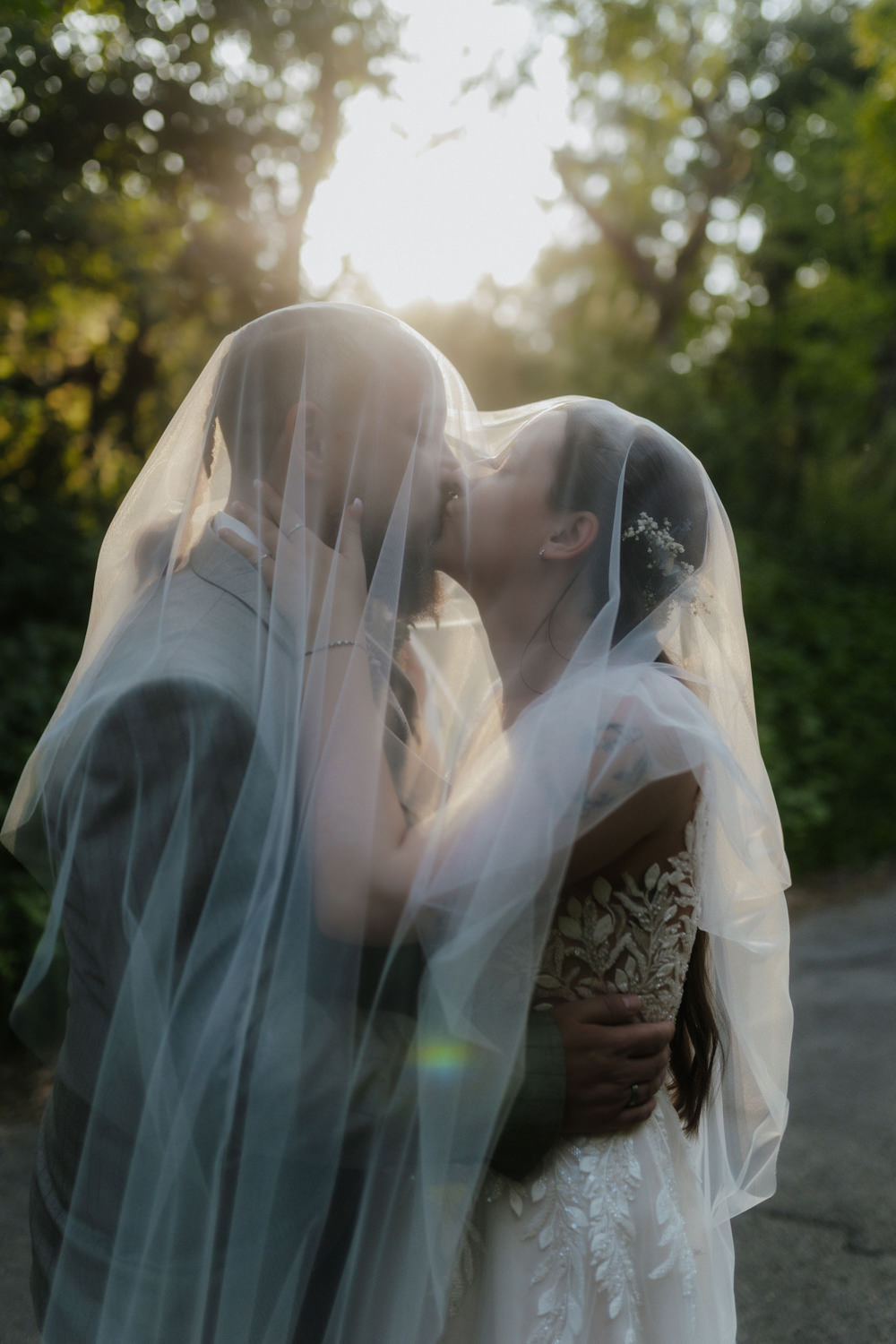 Glückliches Brautpaar küsst sich unter Schleier im Gegenlicht