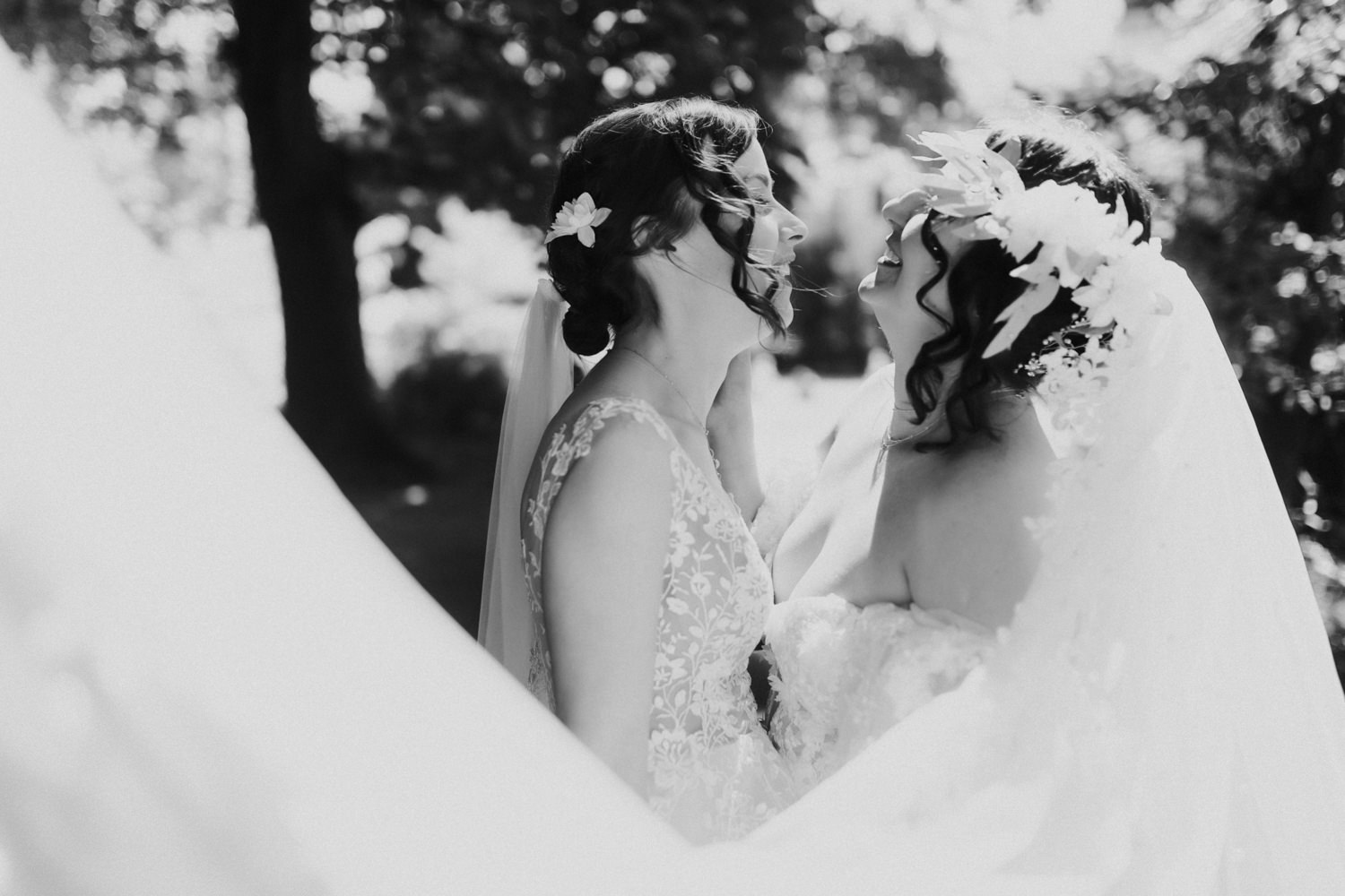 Emotionaler Moment zweier Bräute unter Schleier im Sonnenlicht im Park