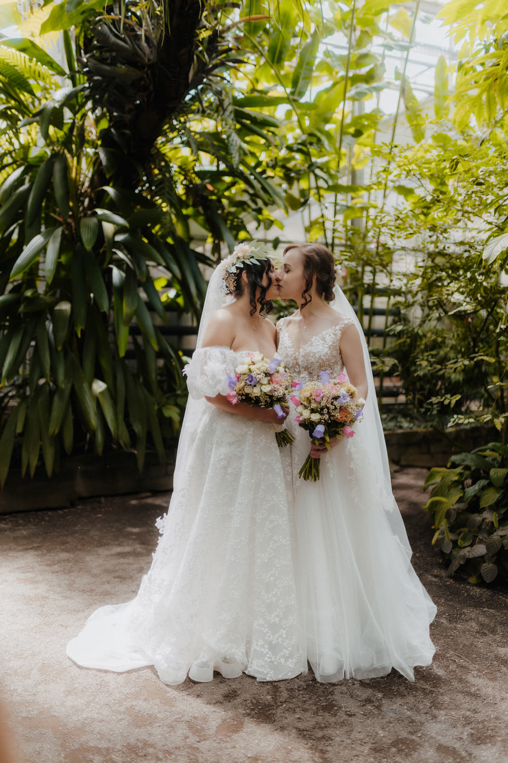 Gleichgeschlechtliche Hochzeit im Gewächshaus, Brautpaar zwischen Palmen küsst sich