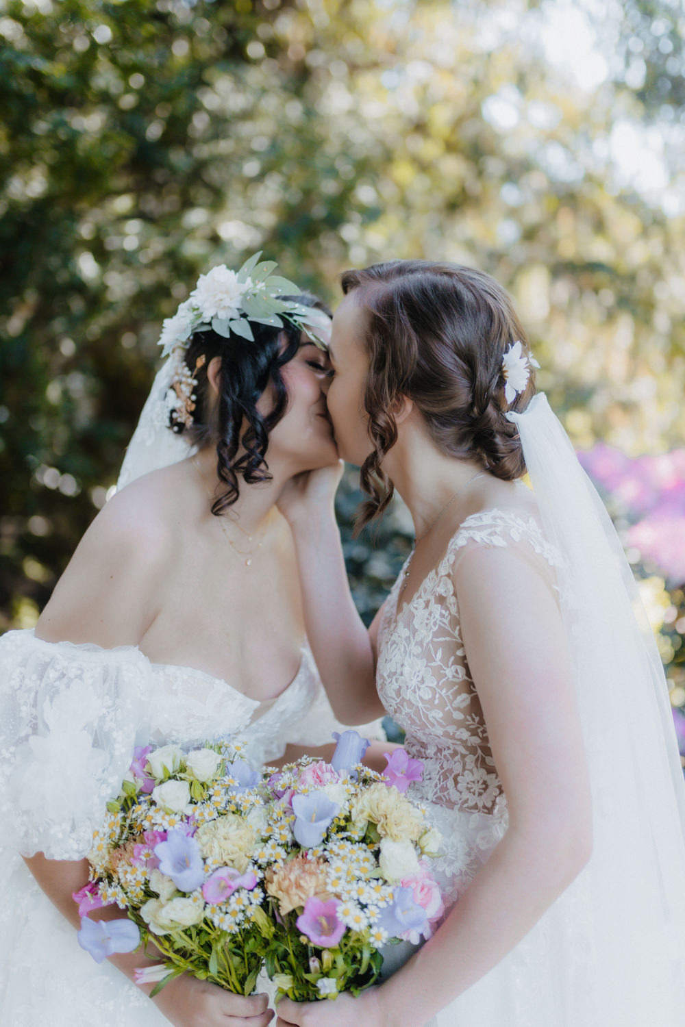 Lesbisches Brautpaar küsst sich mit Blumenstrauß im Park